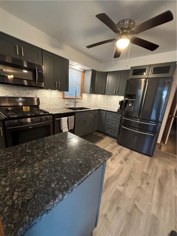 kitchen featuring sink, stainless steel appliances, dark stone counters, decorative backsplash, and light wood-type flooring