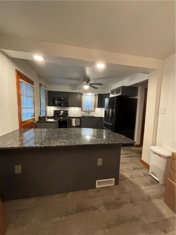 kitchen with dark stone counters, kitchen peninsula, ceiling fan, and stainless steel appliances