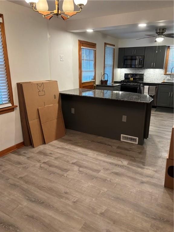 kitchen featuring decorative backsplash, dark stone countertops, black gas range oven, light hardwood / wood-style floors, and kitchen peninsula