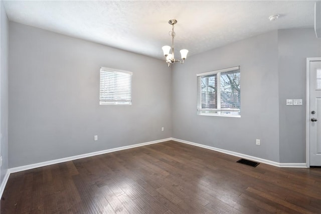 empty room with dark hardwood / wood-style flooring, an inviting chandelier, and plenty of natural light