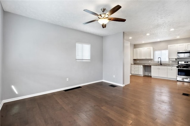 unfurnished living room featuring ceiling fan, sink, dark wood-type flooring, and a textured ceiling