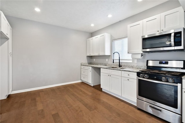 kitchen featuring sink, dark wood-type flooring, light stone counters, white cabinets, and appliances with stainless steel finishes