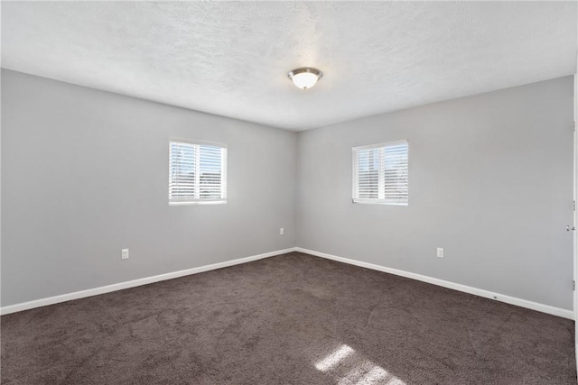 empty room with a healthy amount of sunlight, a textured ceiling, and dark carpet