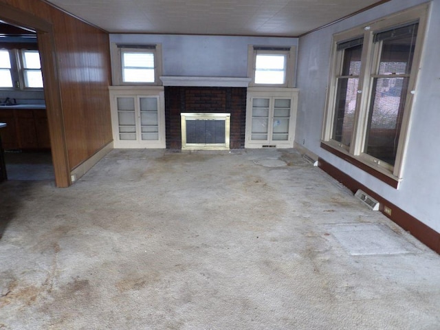 unfurnished living room with wood walls, carpet floors, and a brick fireplace