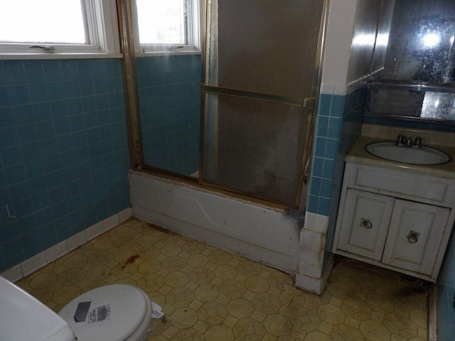 full bathroom with vanity, toilet, tile walls, and bath / shower combo with glass door