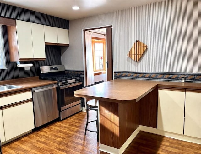 kitchen with stainless steel appliances, sink, light hardwood / wood-style flooring, white cabinetry, and a breakfast bar area