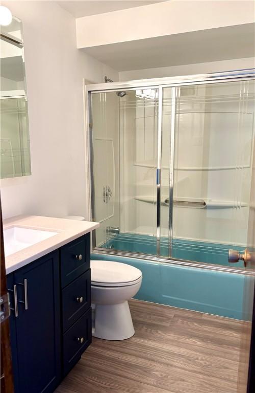 full bathroom featuring vanity, toilet, wood-type flooring, and shower / bath combination with glass door