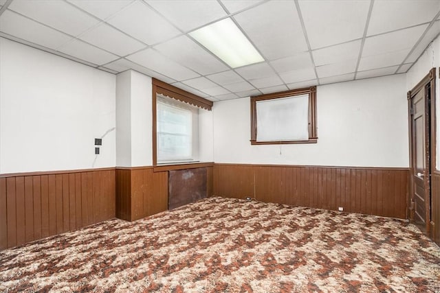 unfurnished room featuring carpet floors, a paneled ceiling, and wood walls