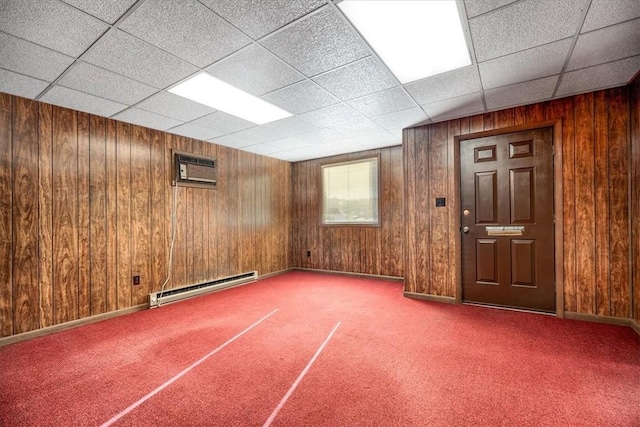 interior space with a wall mounted air conditioner, a drop ceiling, a baseboard heating unit, and wood walls