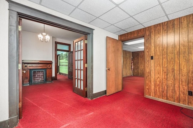 hallway with wood walls, a drop ceiling, dark carpet, and an inviting chandelier