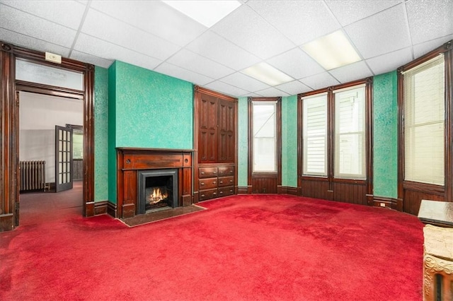 carpeted living room with radiator heating unit and a drop ceiling