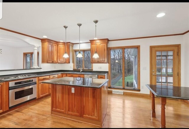 kitchen with hanging light fixtures, stainless steel appliances, crown molding, light hardwood / wood-style floors, and a kitchen island