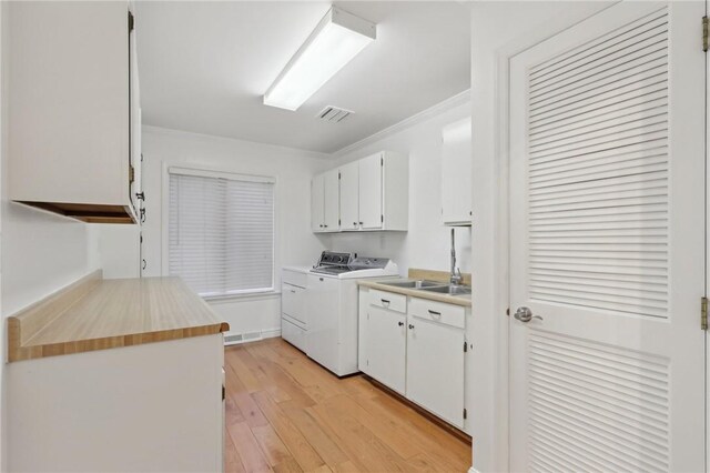 laundry room featuring washing machine and clothes dryer, crown molding, cabinets, and light hardwood / wood-style floors