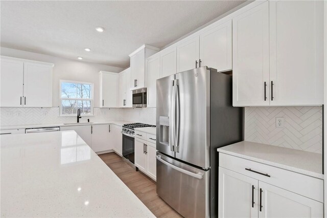 kitchen featuring appliances with stainless steel finishes, white cabinetry, decorative backsplash, sink, and light stone counters