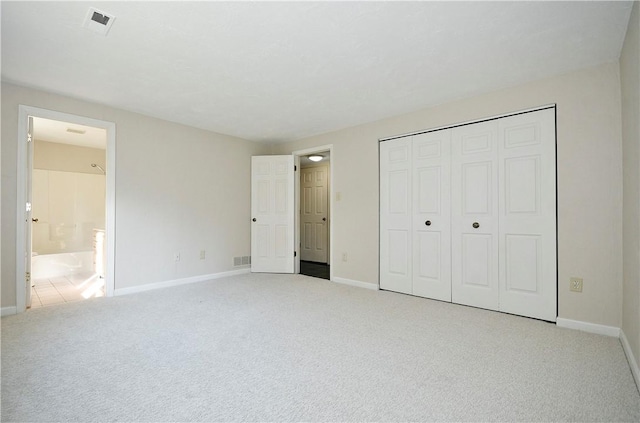 unfurnished bedroom featuring light carpet, ensuite bath, and a closet