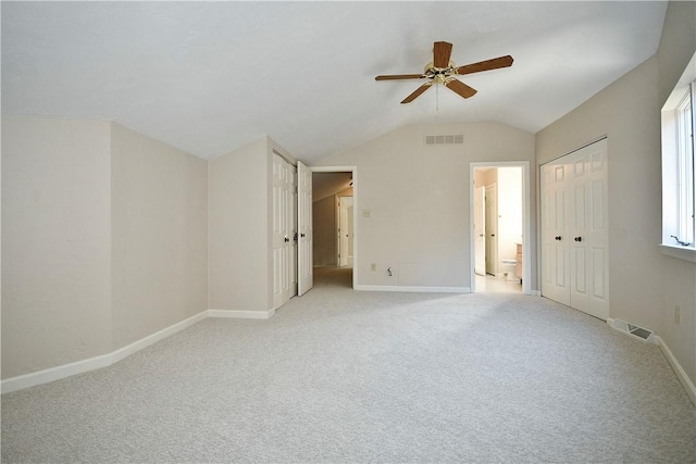 unfurnished bedroom with connected bathroom, light colored carpet, vaulted ceiling, and ceiling fan