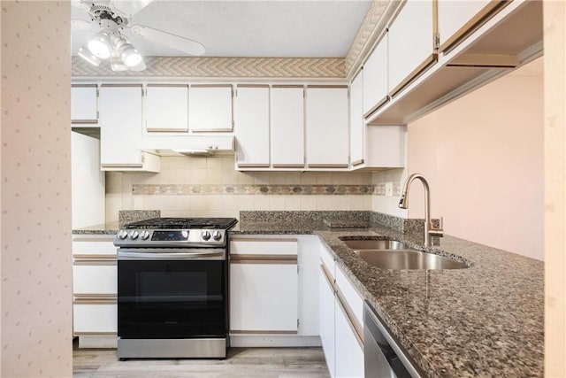 kitchen featuring sink, dark stone countertops, light wood-type flooring, appliances with stainless steel finishes, and white cabinetry