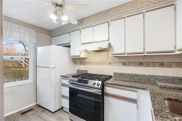 kitchen with stainless steel gas stove, white fridge, white cabinetry, and dark stone counters