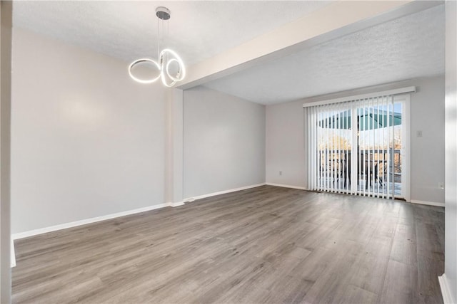 empty room featuring beamed ceiling, a notable chandelier, wood-type flooring, and a textured ceiling