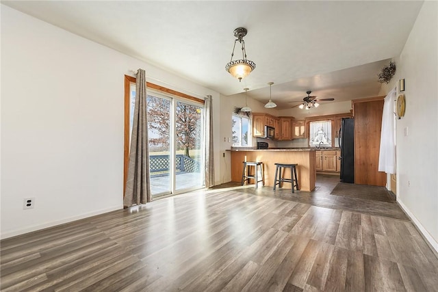 kitchen featuring a breakfast bar, black refrigerator, dark hardwood / wood-style floors, decorative light fixtures, and kitchen peninsula