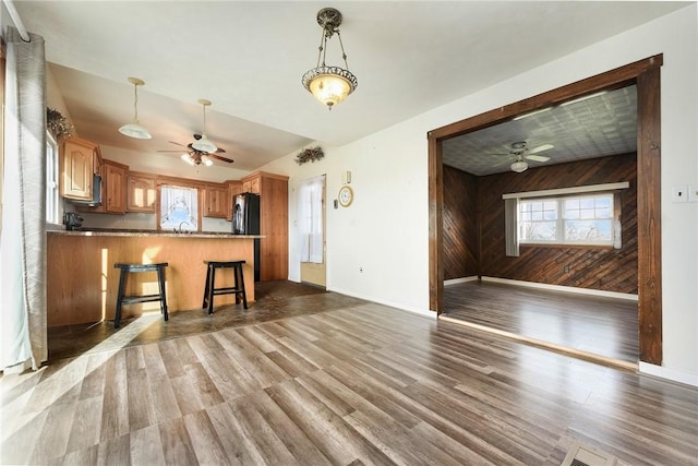 kitchen featuring dark wood-type flooring, black fridge, wooden walls, a kitchen bar, and kitchen peninsula