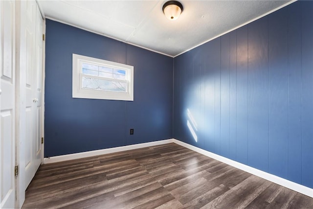 empty room featuring crown molding, dark wood-type flooring, and wood walls