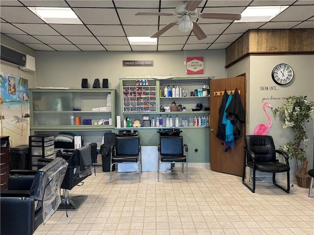 interior space with a wall mounted AC, ceiling fan, and a drop ceiling