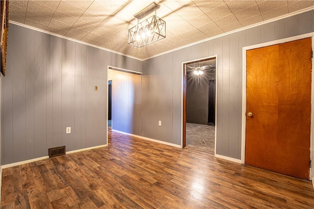 empty room featuring ornamental molding, wooden walls, dark wood-type flooring, and a notable chandelier