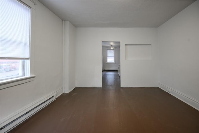 unfurnished room featuring dark hardwood / wood-style floors, baseboard heating, and a wealth of natural light