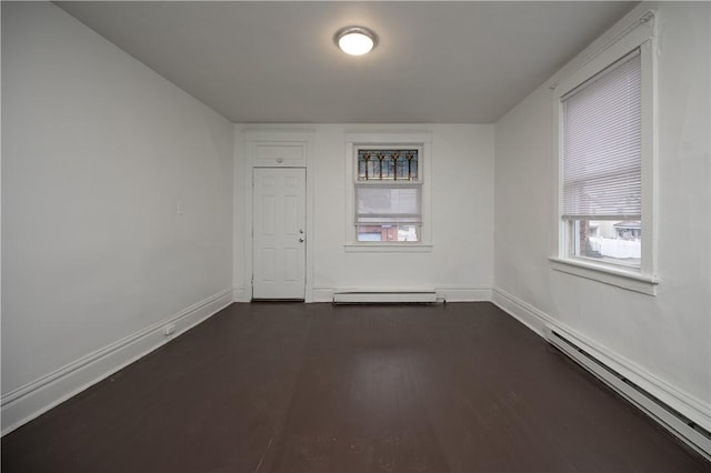 empty room with dark hardwood / wood-style flooring, a healthy amount of sunlight, and a baseboard heating unit