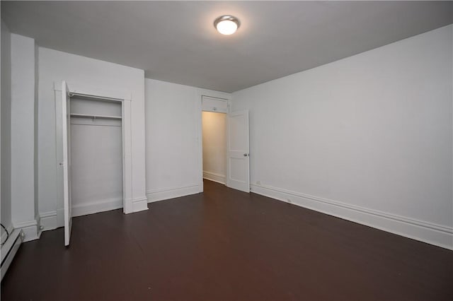 unfurnished bedroom with dark hardwood / wood-style floors, a baseboard radiator, and a closet