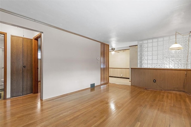 unfurnished room with wood walls, ceiling fan, ornamental molding, and light wood-type flooring