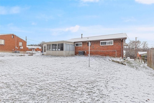 snow covered house featuring a sunroom and central AC unit