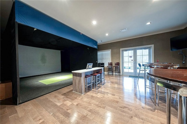 kitchen featuring french doors, ornamental molding, light hardwood / wood-style flooring, golf simulator, and a breakfast bar area