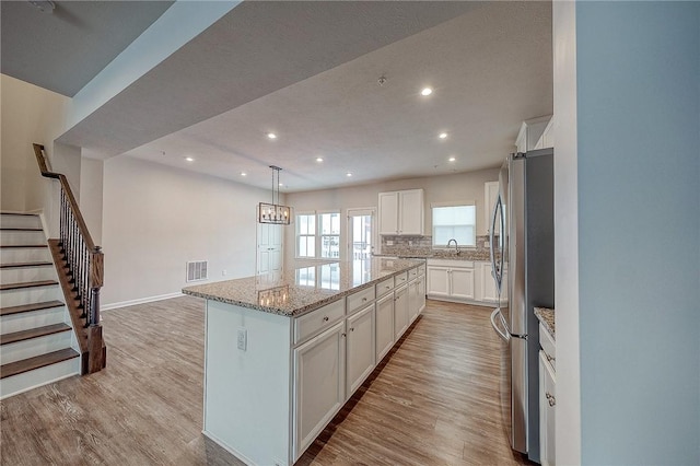 kitchen featuring stainless steel refrigerator, white cabinetry, hanging light fixtures, light hardwood / wood-style floors, and a kitchen island