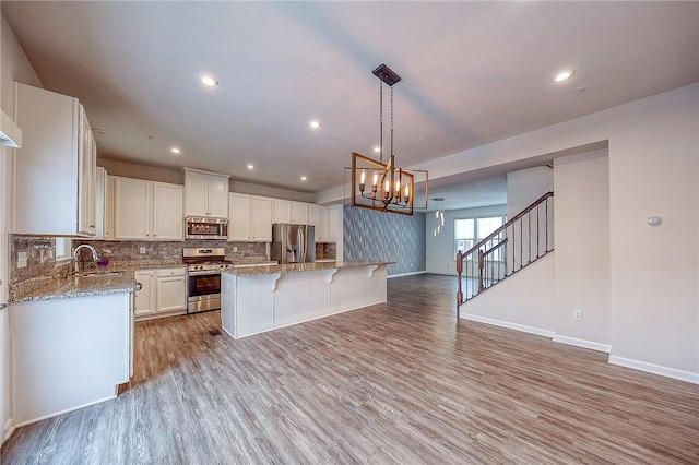 kitchen featuring appliances with stainless steel finishes, light wood-type flooring, an inviting chandelier, white cabinets, and a center island