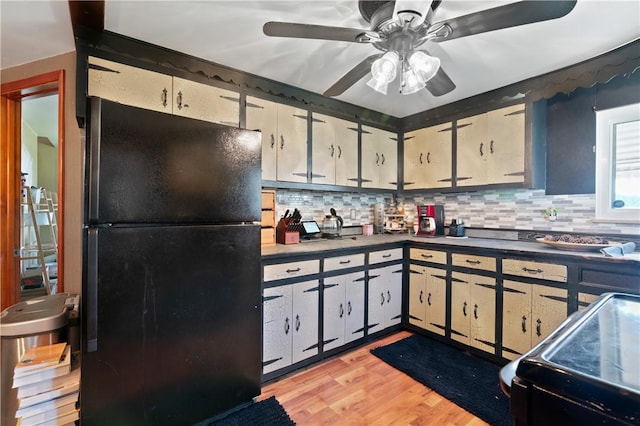 kitchen featuring stove, backsplash, black refrigerator, light hardwood / wood-style flooring, and ceiling fan