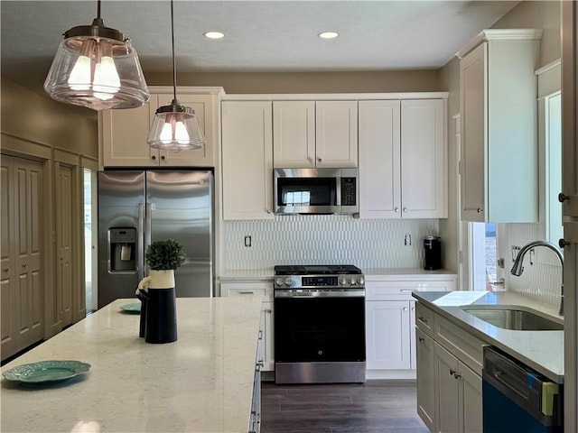 kitchen with stainless steel appliances, a sink, hanging light fixtures, and light stone countertops