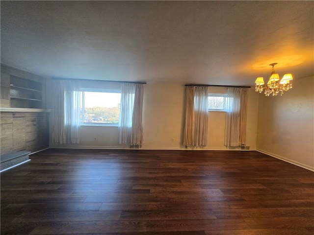 spare room featuring a tile fireplace, a chandelier, dark hardwood / wood-style flooring, and a healthy amount of sunlight