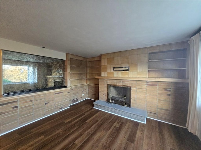 unfurnished living room with built in shelves, dark hardwood / wood-style flooring, and a brick fireplace