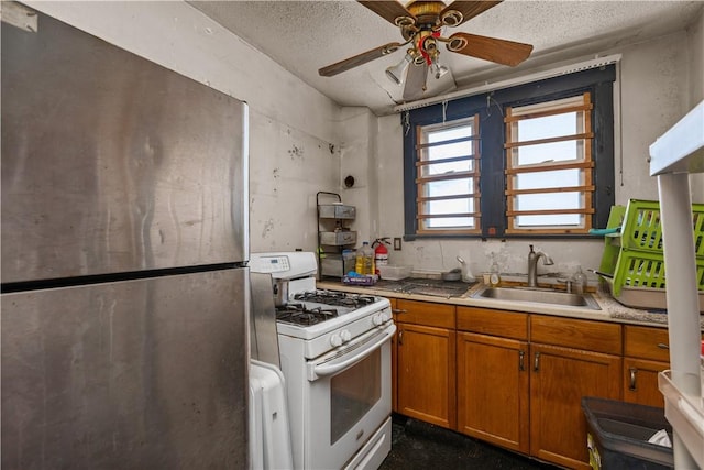 kitchen with white gas range oven, a textured ceiling, ceiling fan, sink, and stainless steel refrigerator