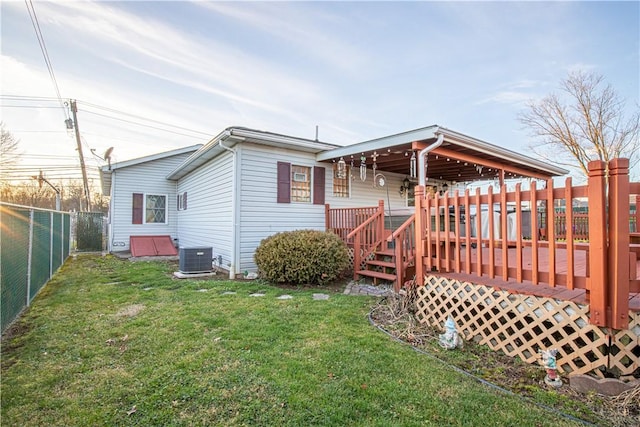 back of property with central AC, a deck, and a lawn