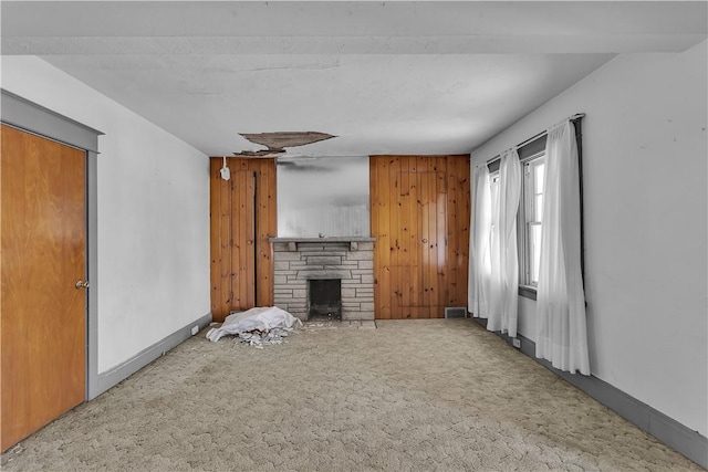 living room with carpet flooring, a stone fireplace, and wooden walls