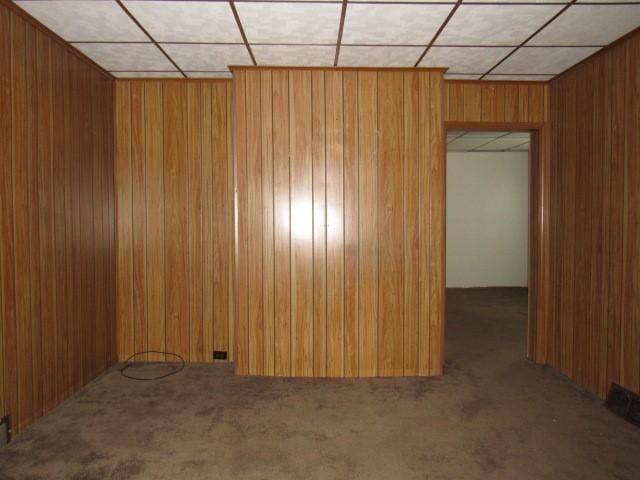 carpeted empty room with a paneled ceiling and wooden walls