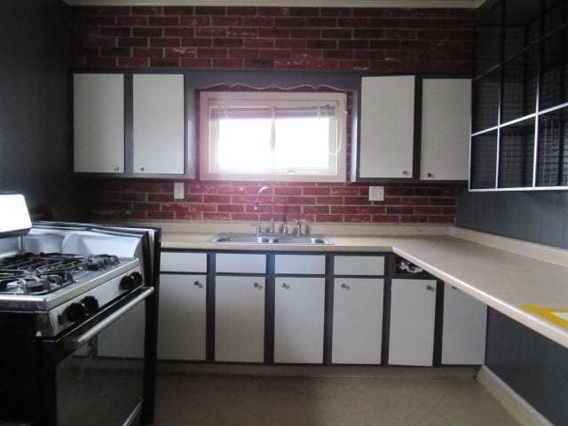 kitchen with backsplash, white cabinetry, white gas range, and sink