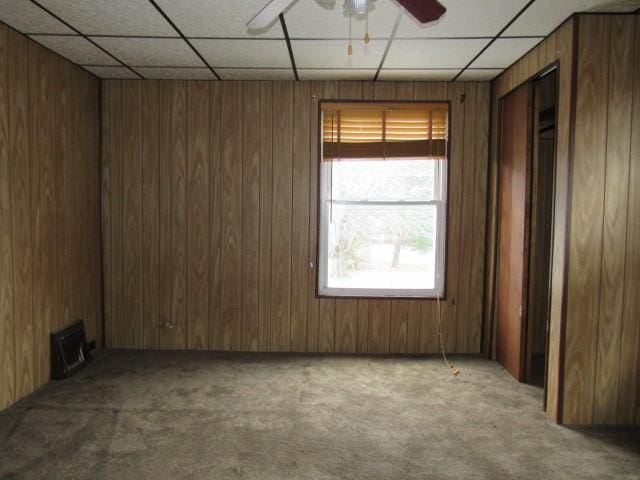 carpeted spare room featuring ceiling fan, a drop ceiling, and wooden walls