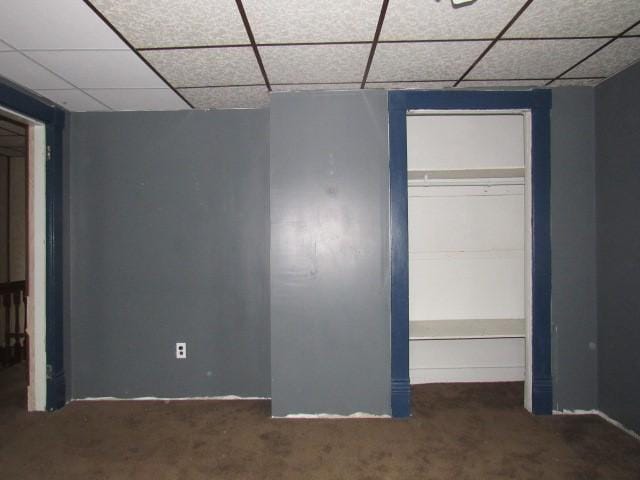 unfurnished bedroom featuring dark colored carpet, a paneled ceiling, and a closet