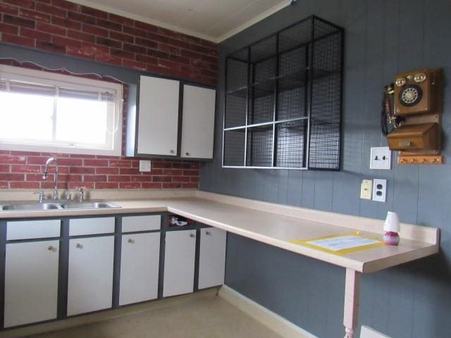 kitchen with white cabinetry, sink, brick wall, and ornamental molding