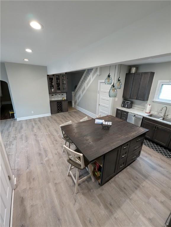 kitchen featuring sink, stainless steel dishwasher, light hardwood / wood-style floors, decorative light fixtures, and dark brown cabinets