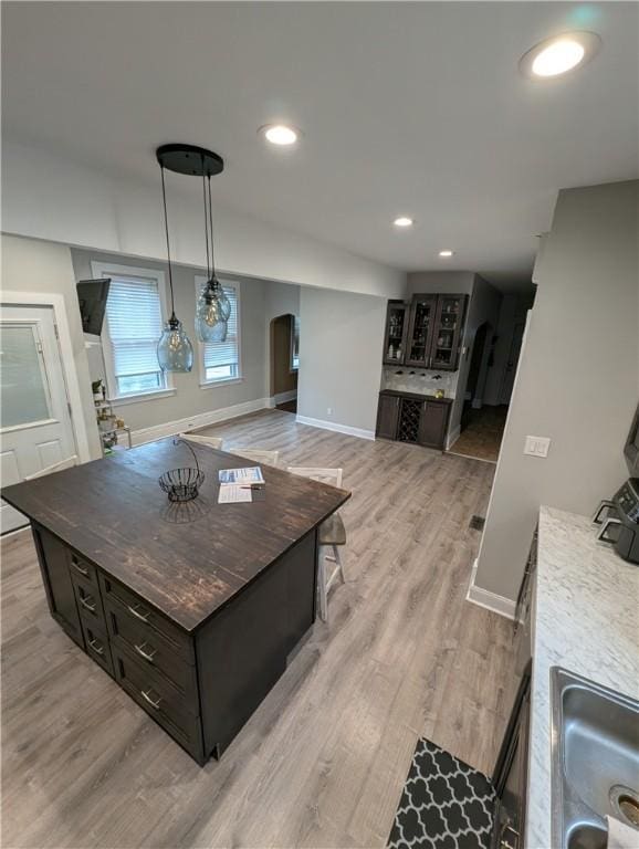 kitchen with pendant lighting, a center island, sink, light hardwood / wood-style flooring, and dark brown cabinets